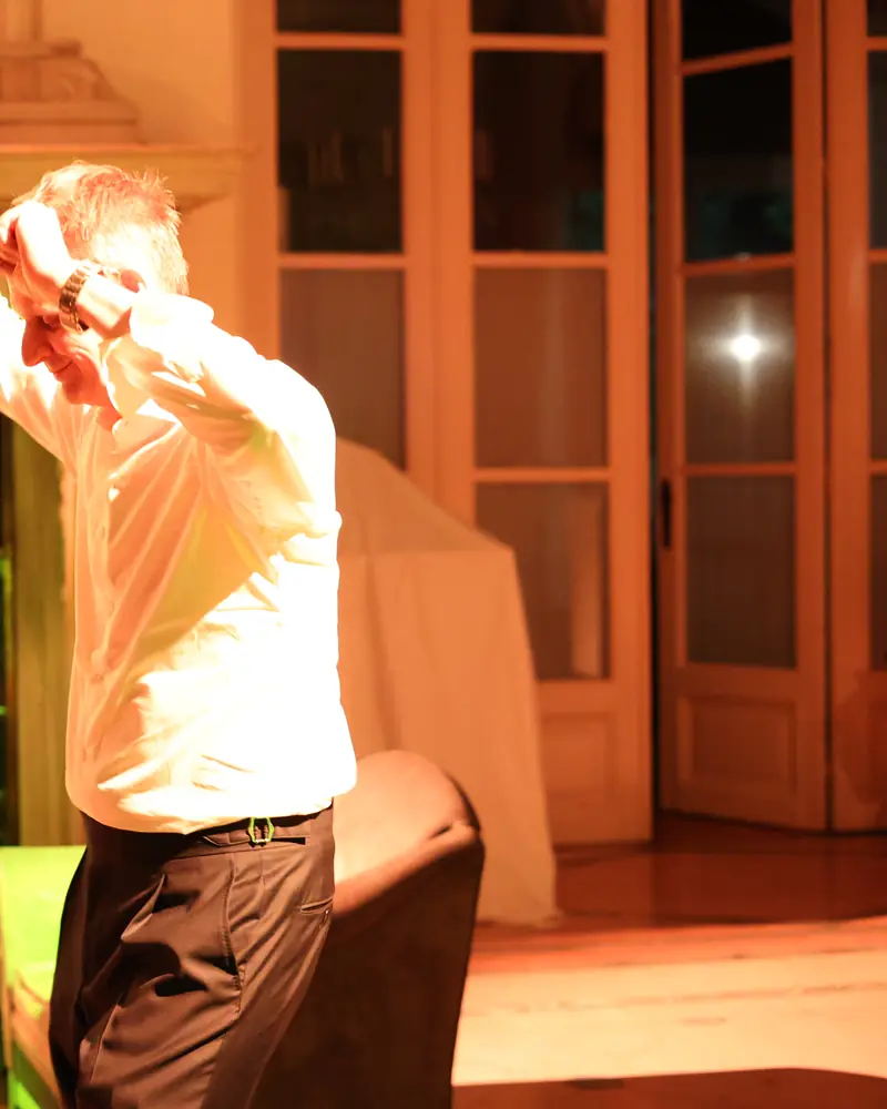 Een gast danst met de arm omhoog, in tegenlicht onder oranje licht (foto Vally Photography)