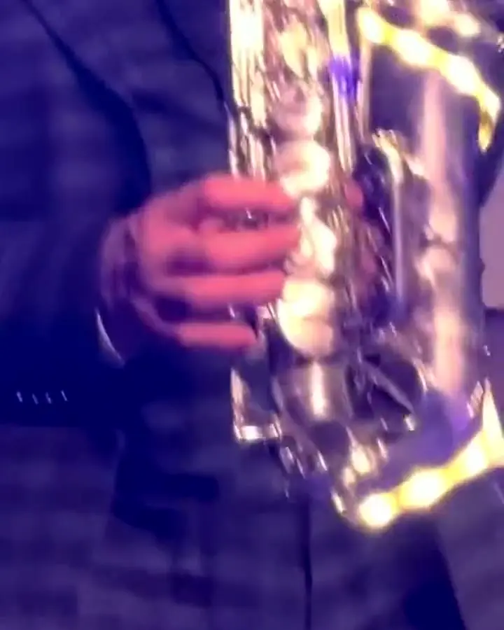 A close-up of a saxophone in the musician’s hands, in front of illuminated letters