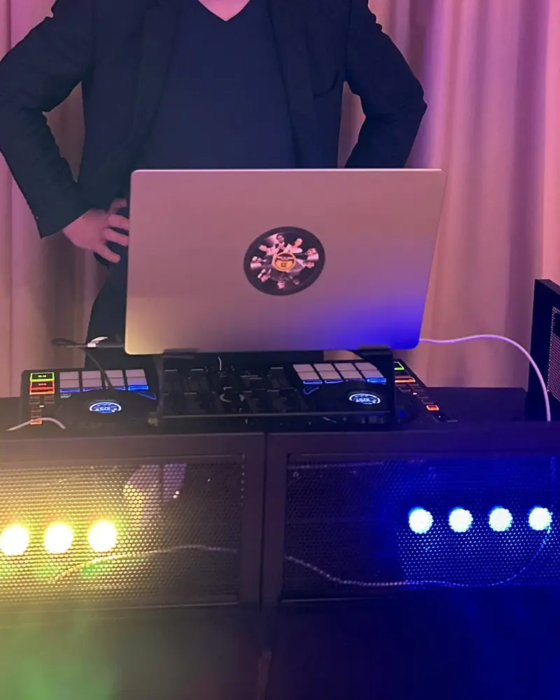 A DJ booth set up in a function room: laptop, controller and LED bars