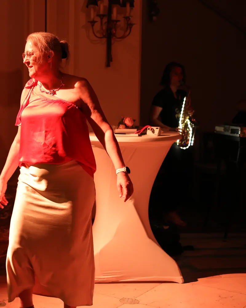 A guest dancing in orange light, the saxophonist playing in the background (photo by Vally Photography)