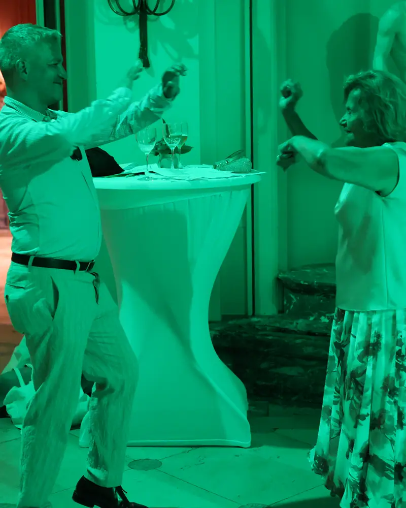 Twee gasten dansen onder groen licht, met een beeld achter hen (foto Vally Photography)