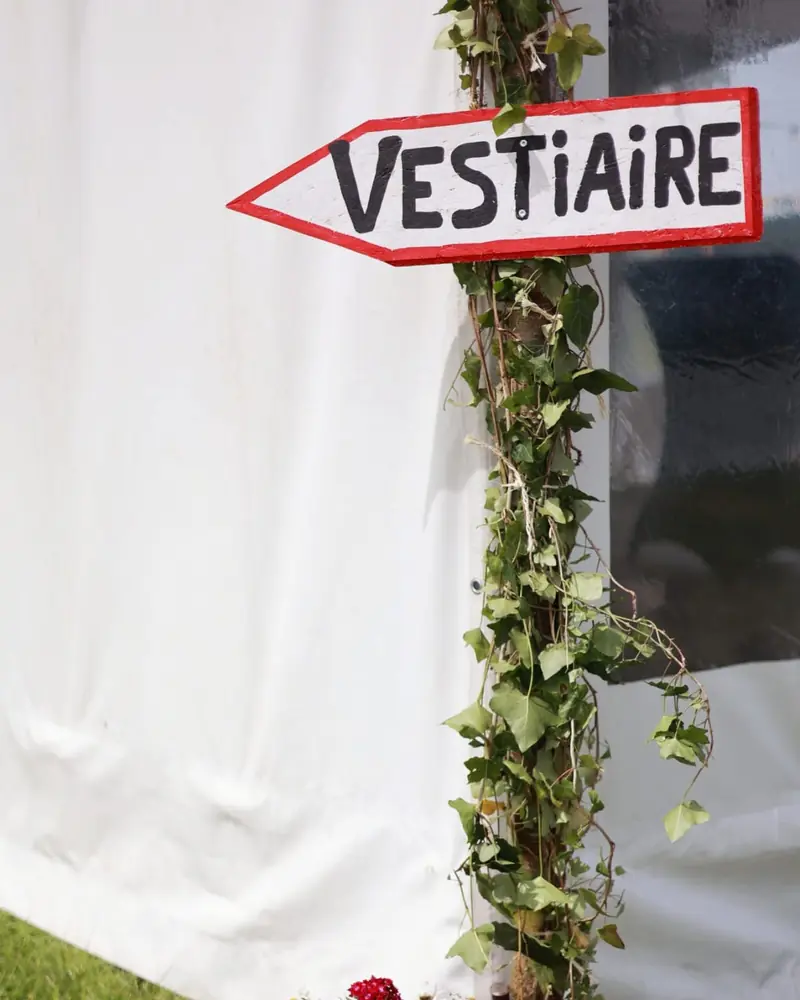 A hand-painted “Vestiaire” (cloakroom) sign wrapped in ivy, by a marquee (photo by Vally Photography)