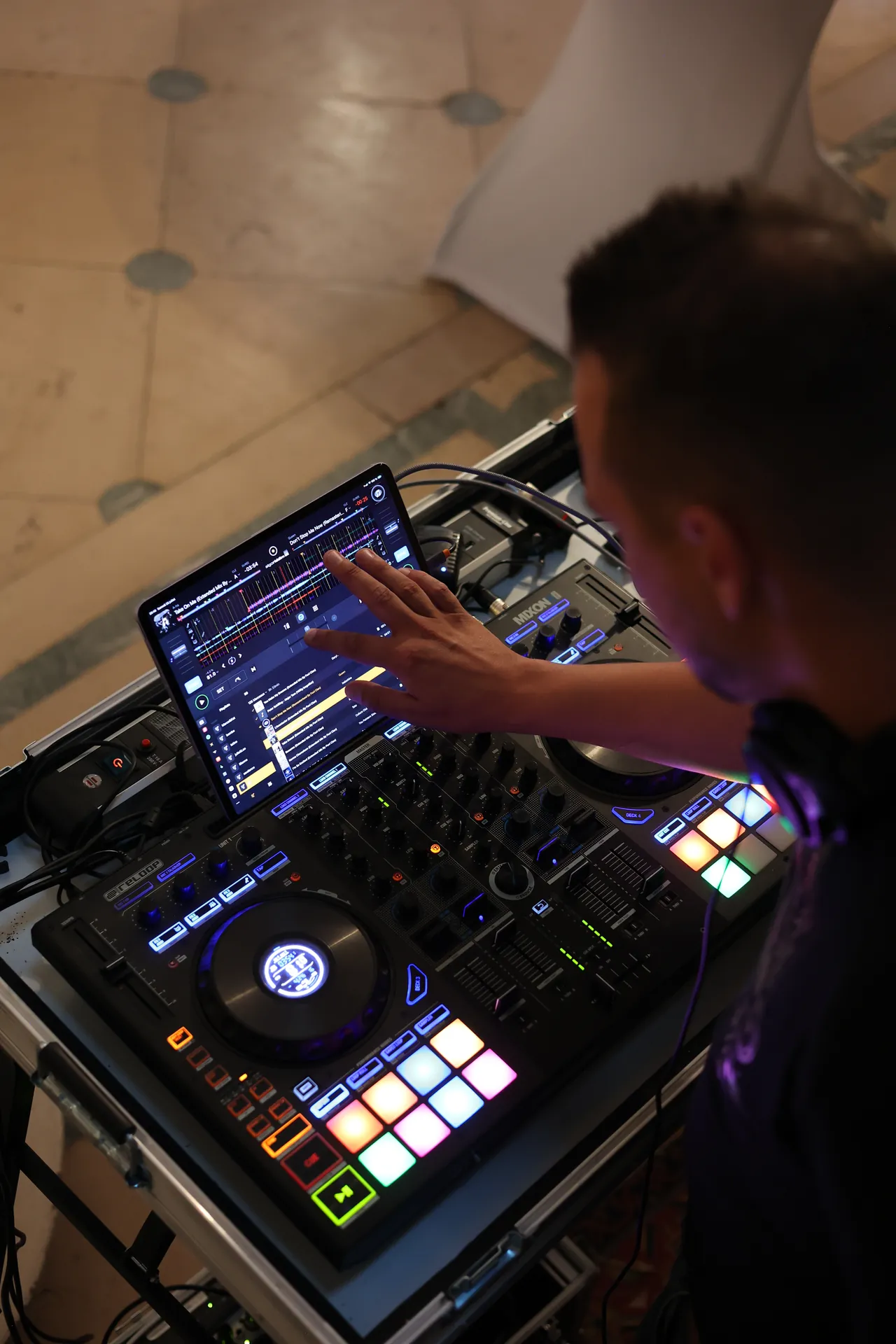 Van bovenaf: de DJ stelt de mix bij op het aanraakscherm, met veelkleurige pads die oplichten
