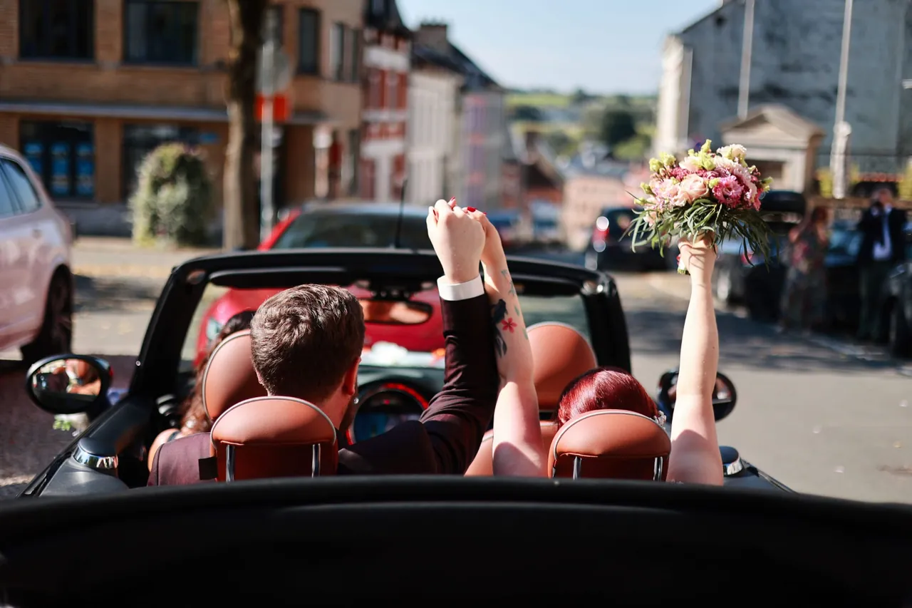 Le couple, bras levés, dans un cabriolet décapoté