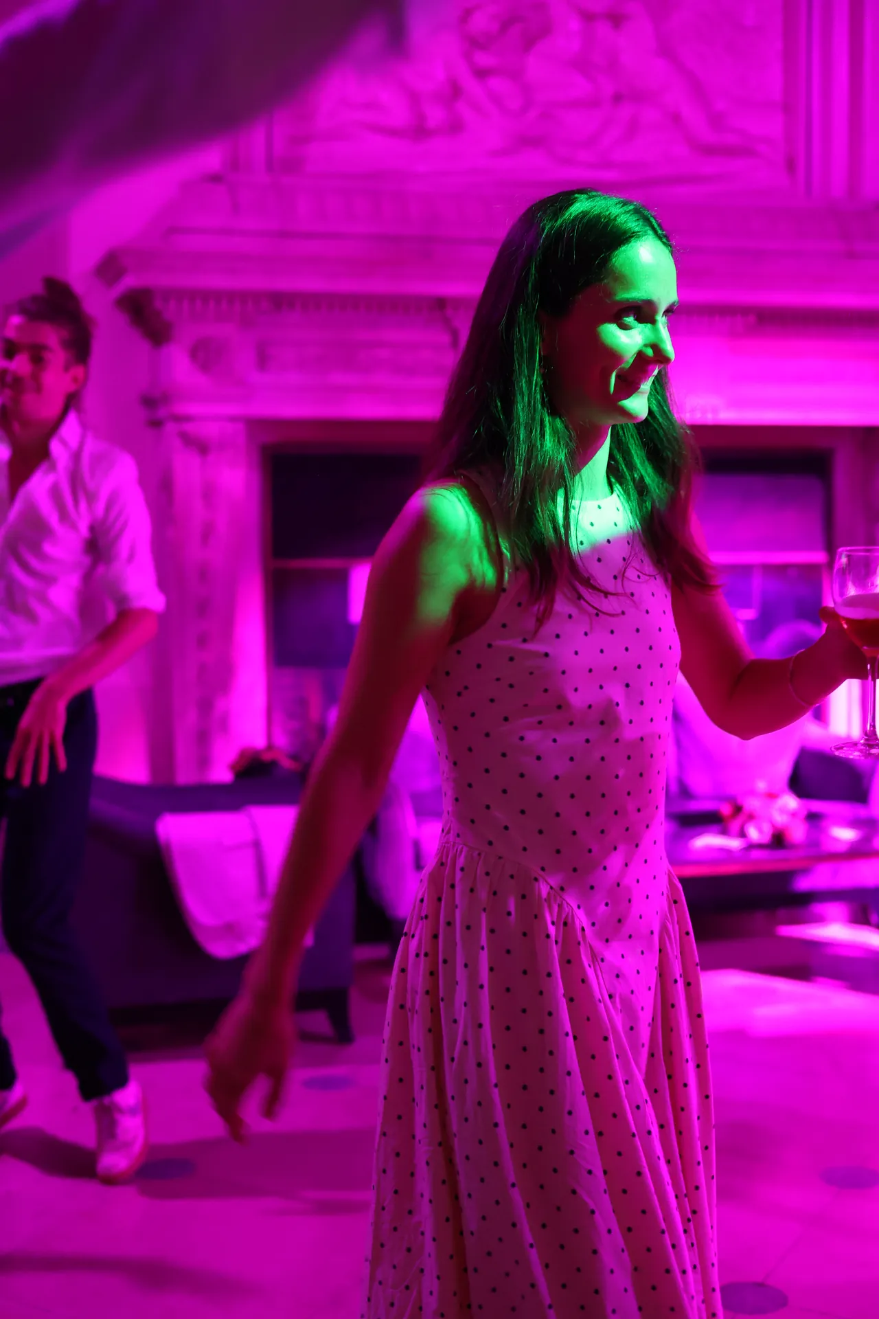 In een jurk met stippen, een glas in de hand: dansen in profiel, in magenta licht