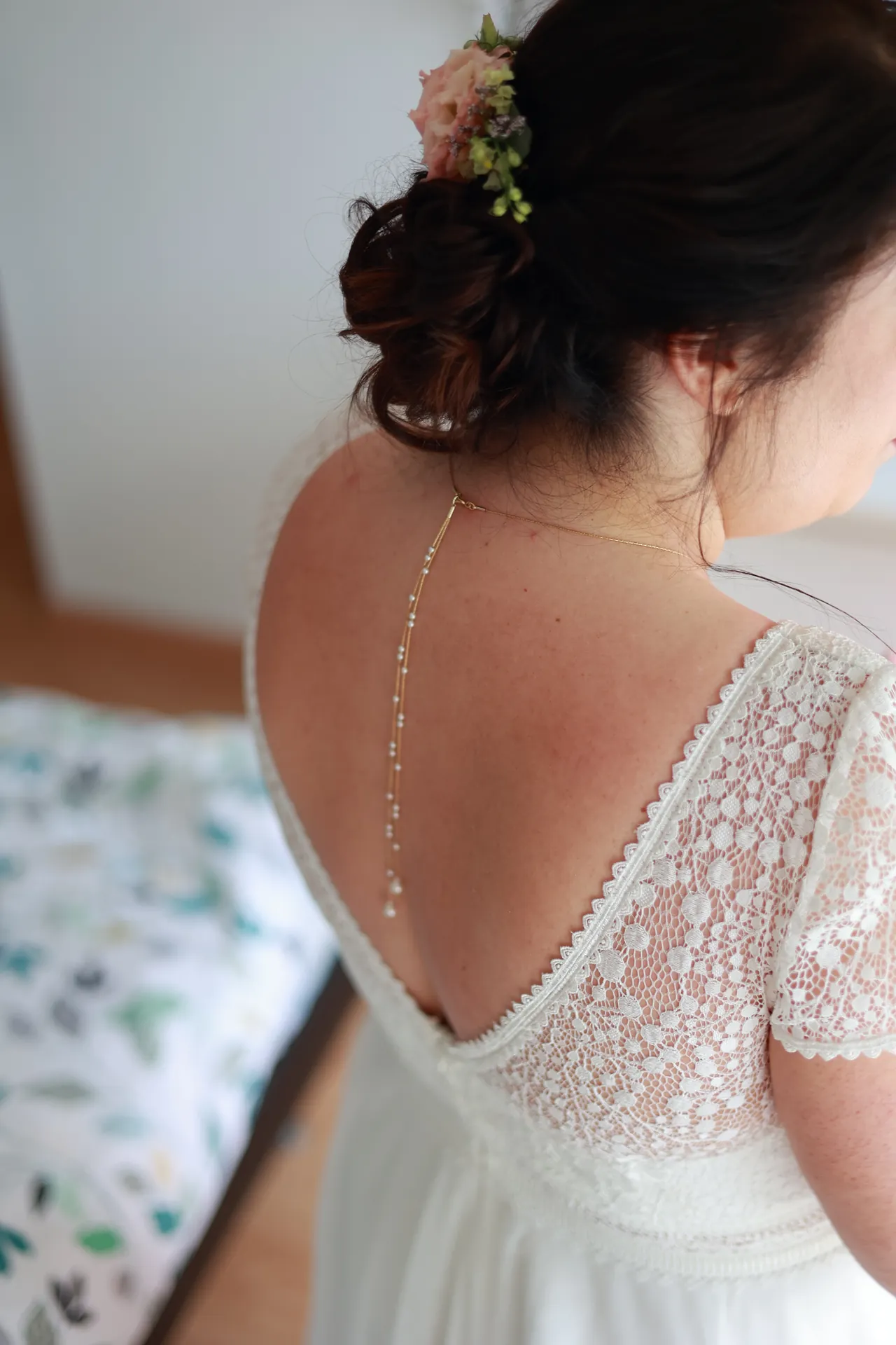Le dos en dentelle de la robe, un bijou de dos et des fleurs dans le chignon