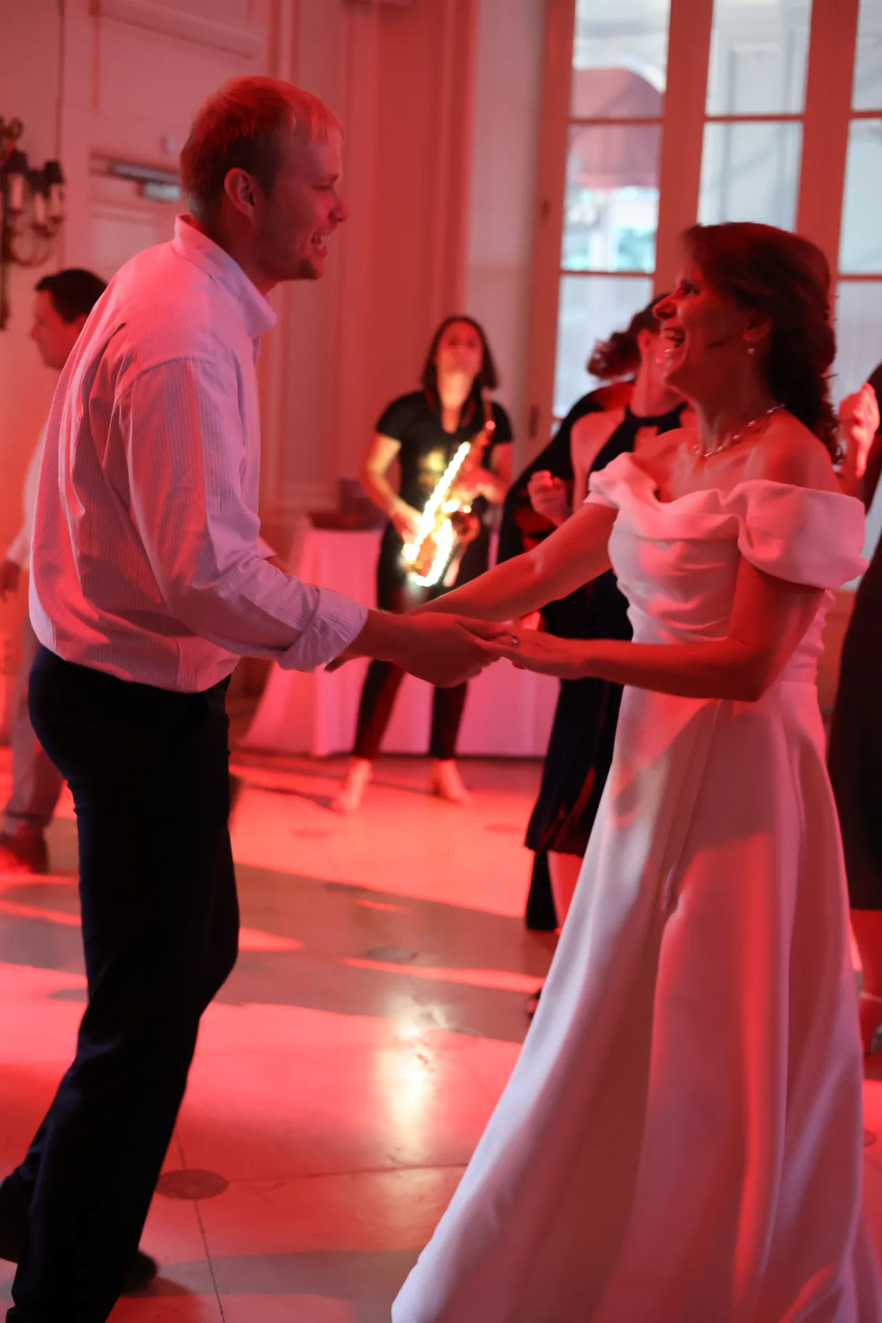 Een schaterlach in een witte jurk, hand in hand in rood licht, de lichtgevende saxofoon op de achtergrond