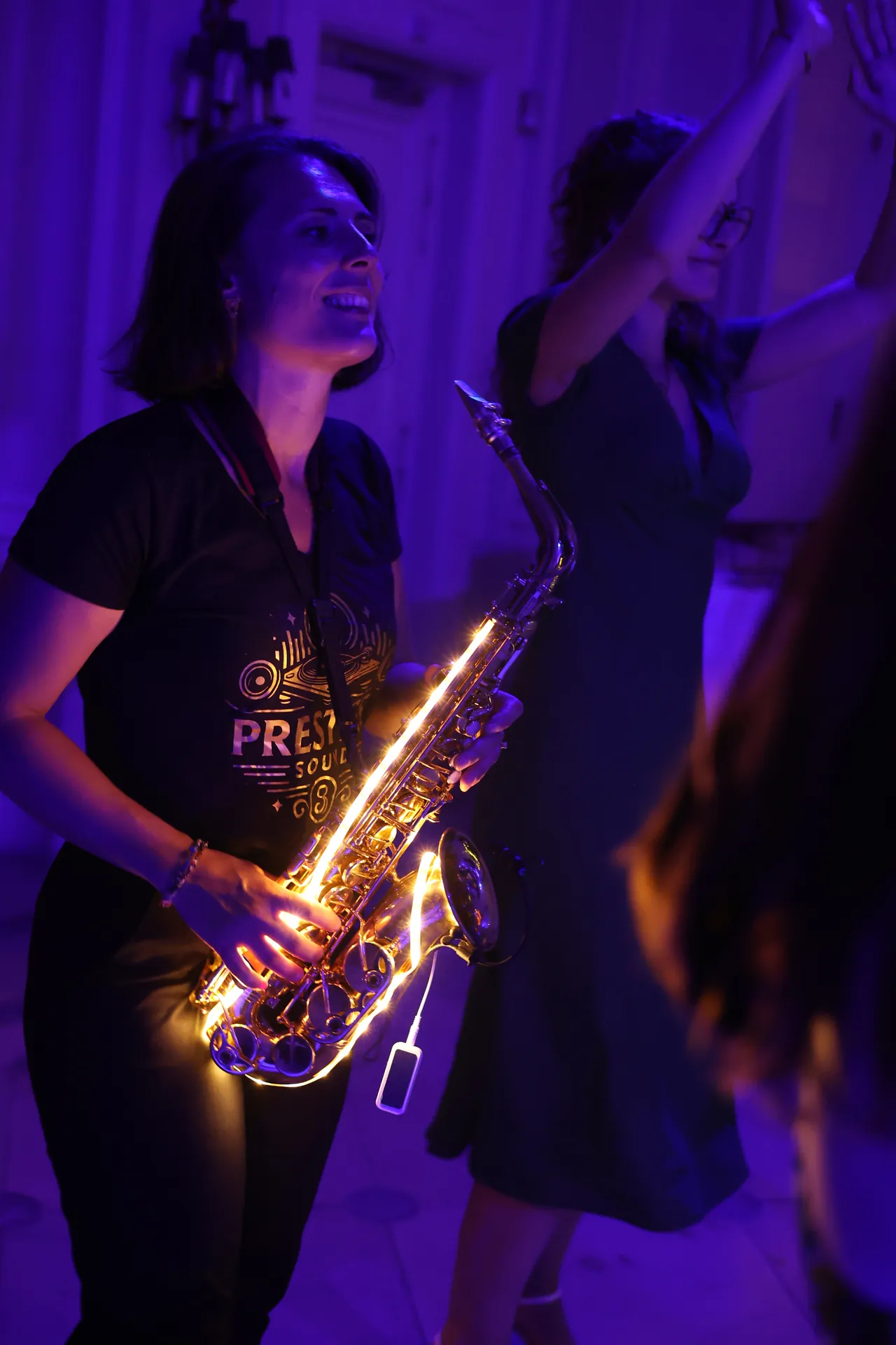 Lichtgevende saxofoon en een brede glimlach tussen de dansers, in paars licht