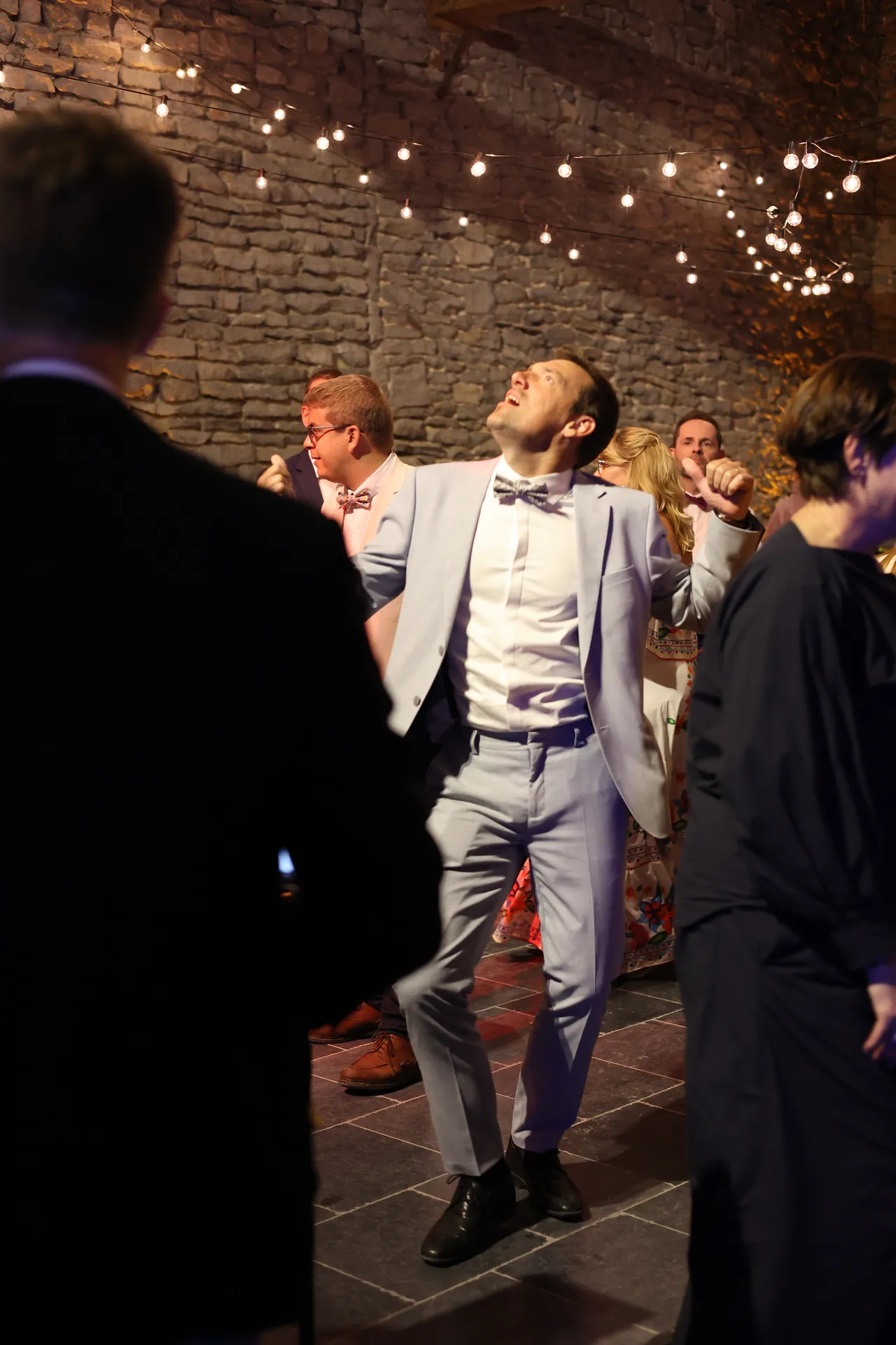 Hoofd achterover en een glimlach: dansen in een licht pak onder de lichtslingers, voor een stenen muur