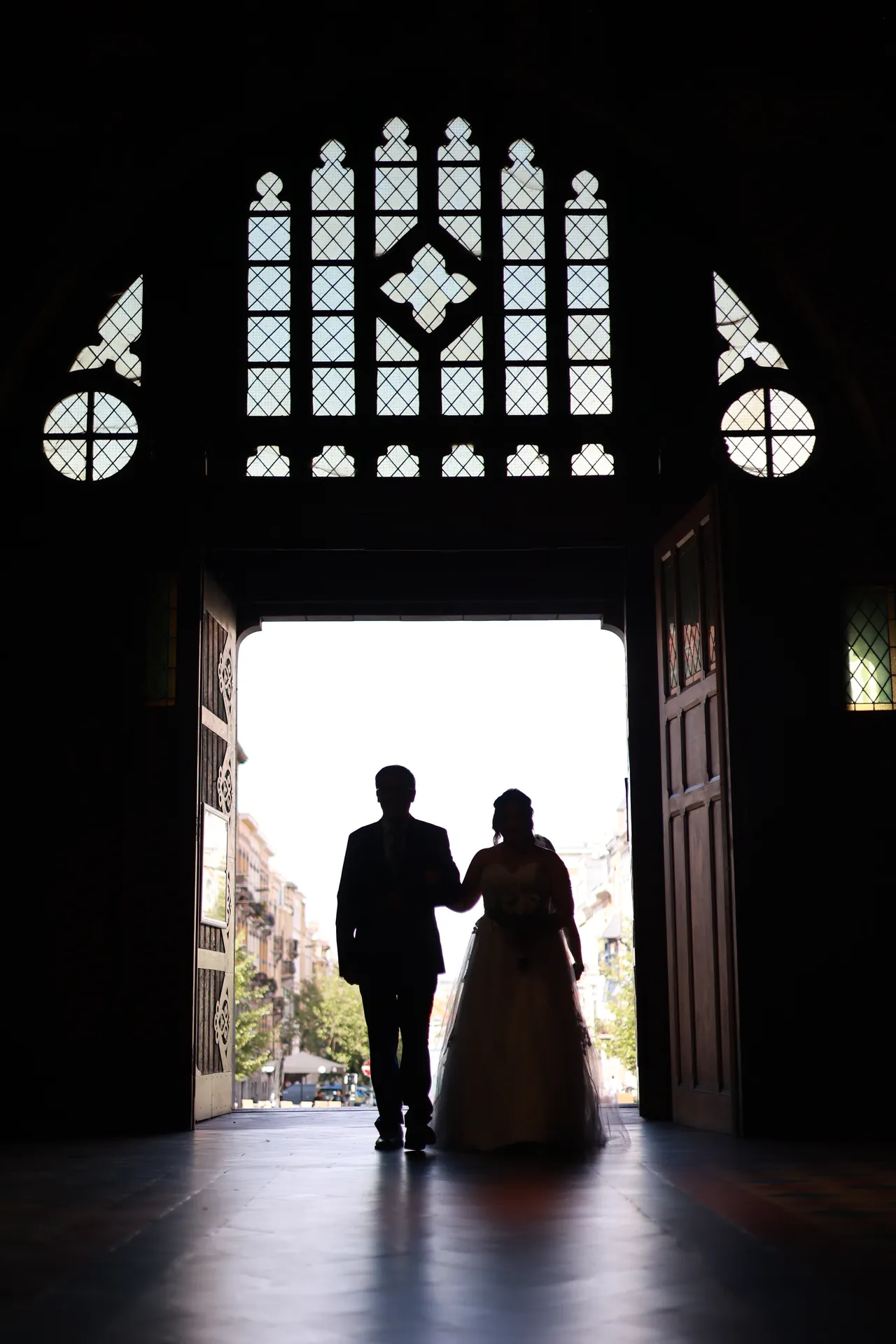 Twee silhouetten arm in arm in het portaal van een kerk, onder een groot glasraam